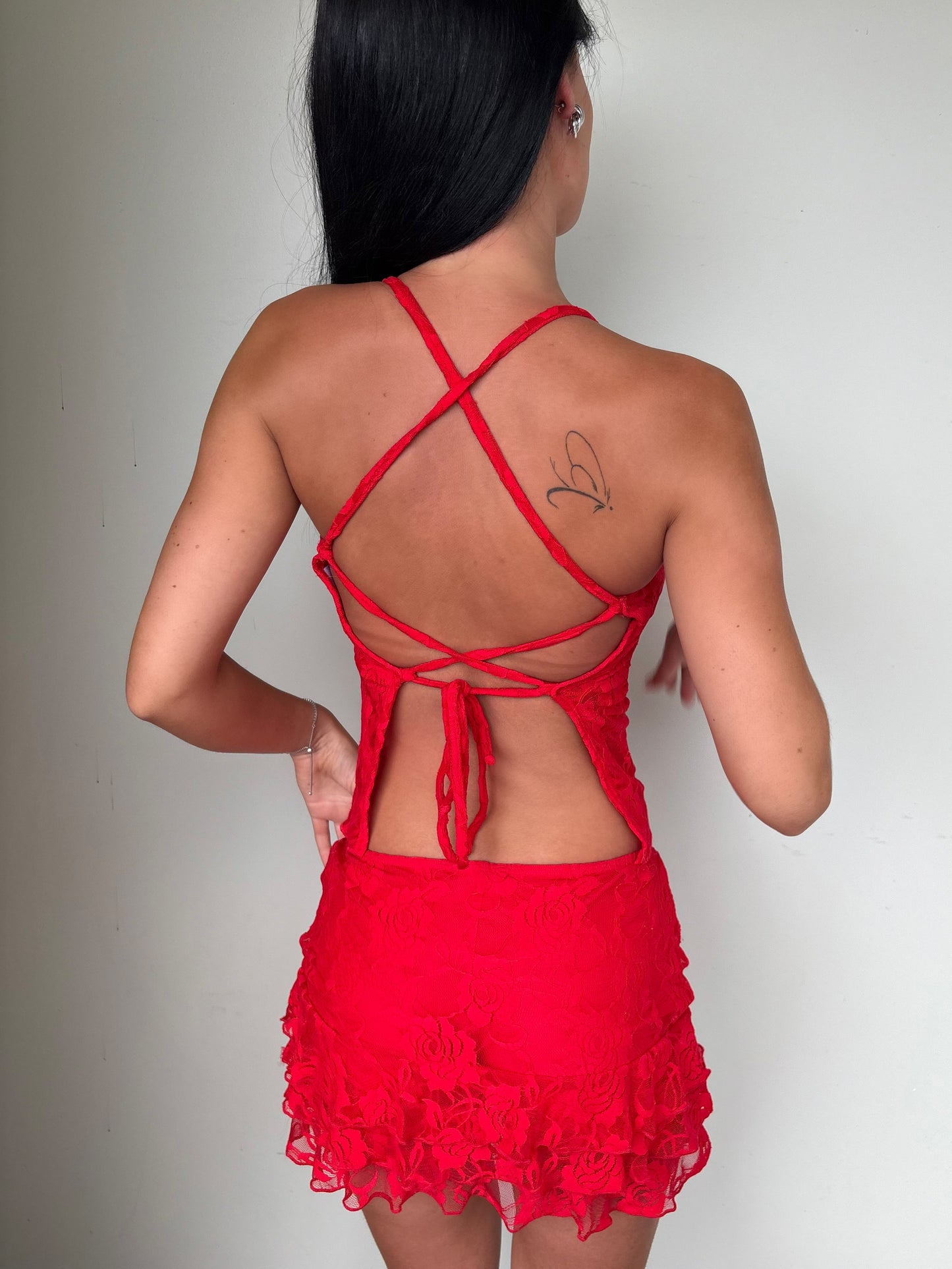 Model wearing a matching red lace set from Yasmin The Label featuring a top with adjustable ties and mini skirt with built-in shorts; triple-layered lace on bust area for coverage, double-layered throughout; model is size 6 and wears XS/S.