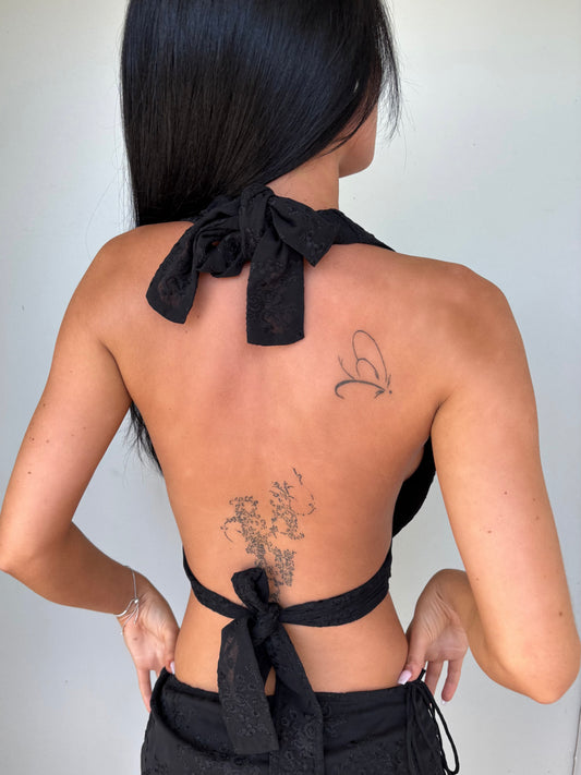 Model wearing a black scoop neck top from Yasmin The Label featuring adjustable ties at the top and back; classic design shown on model who is a size 6 and wears XS/S.