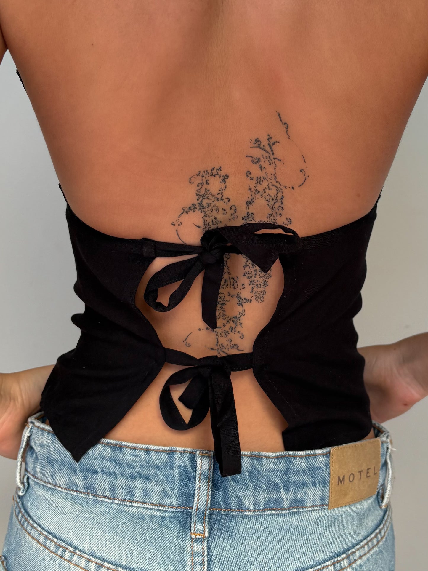 Model wearing a black lace halter top from Yasmin The Label featuring adjustable ties at the top and back; intricate design shown on model who is an Australian size 6 and wears XS/S.