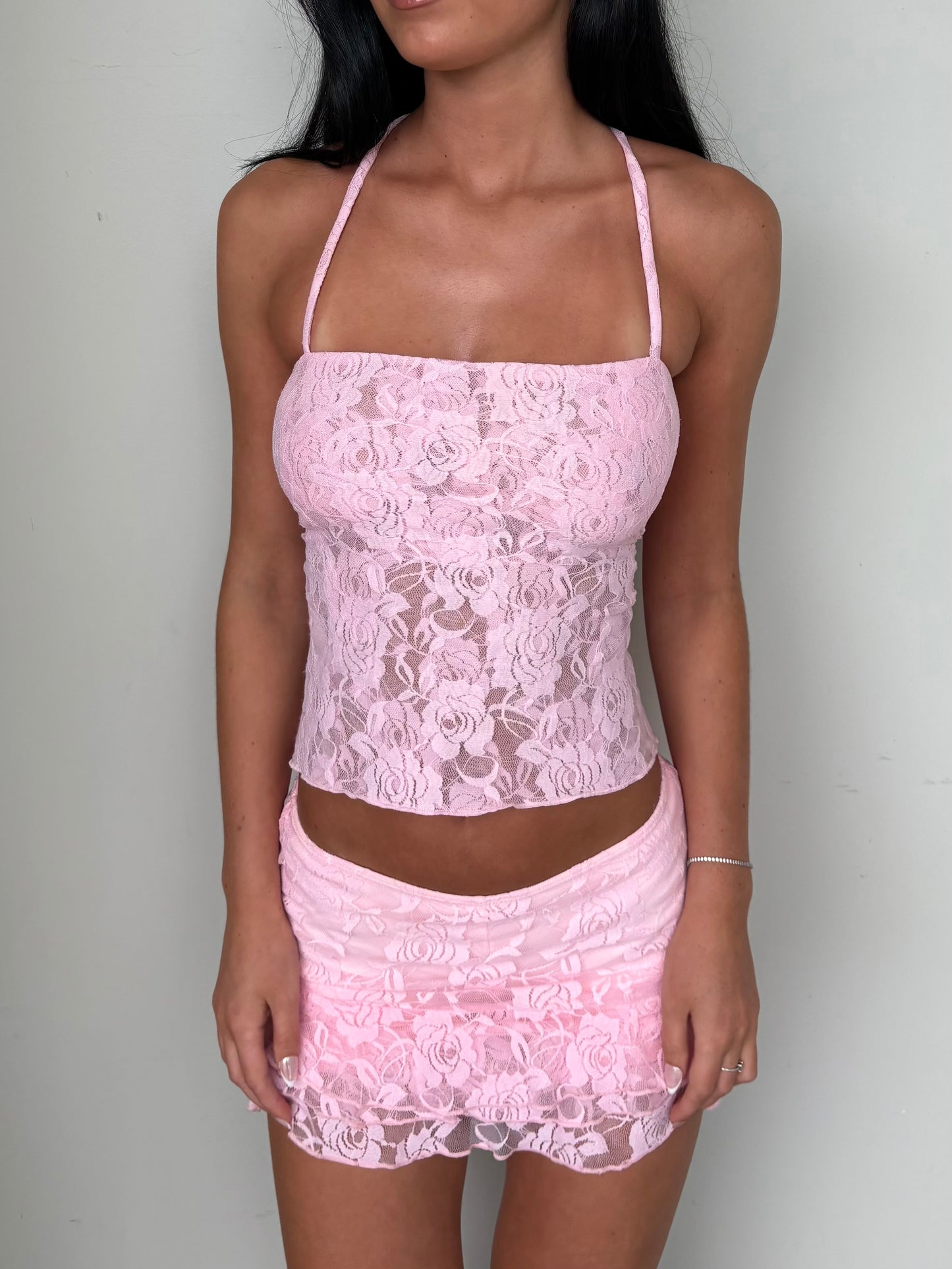 Model wearing a matching baby pink lace set from Yasmin The Label featuring a top with adjustable ties and mini skirt with built-in shorts; triple-layered lace on bust area for coverage, double-layered throughout; model is size 6 and wears XS/S.