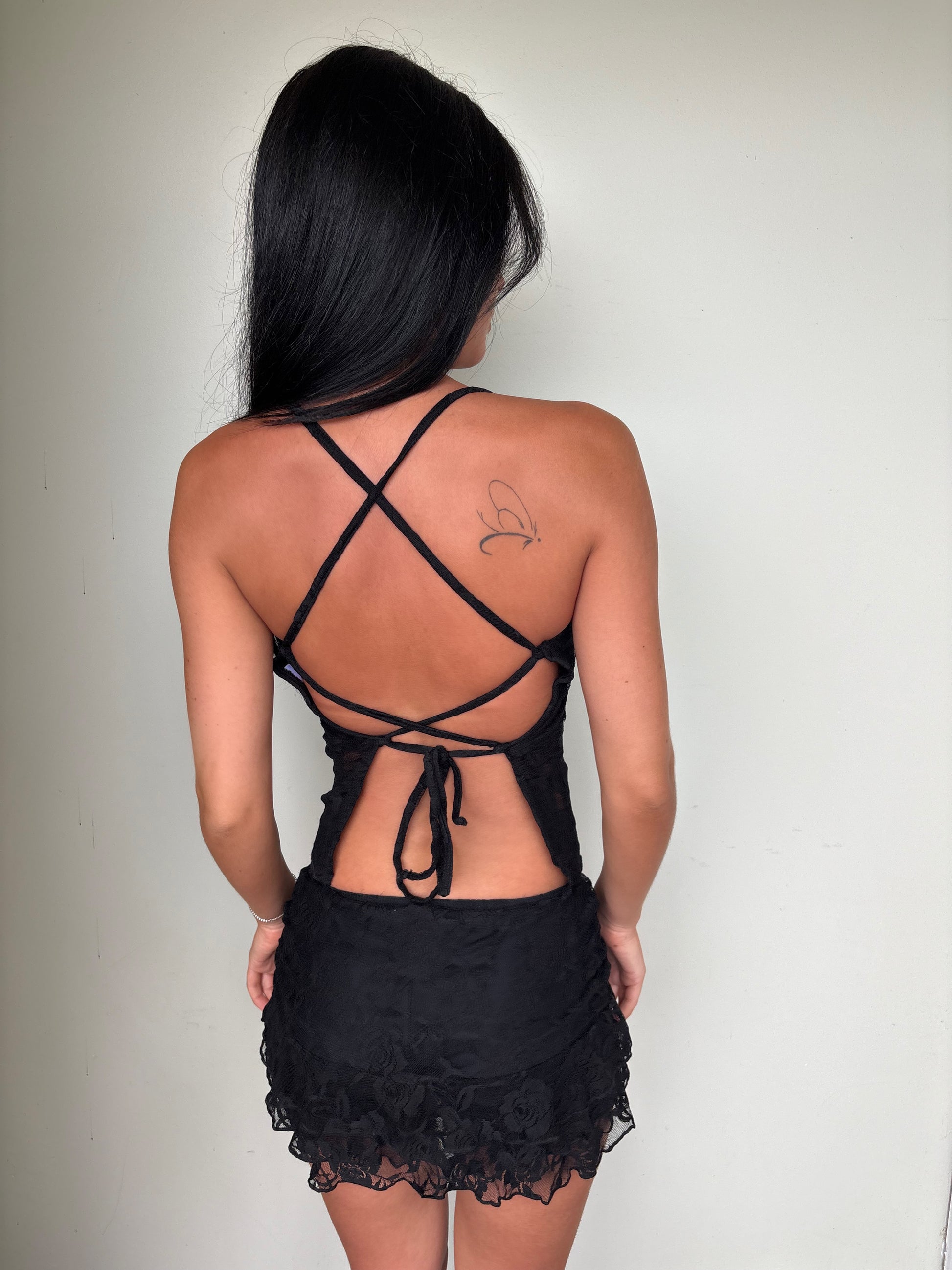 Model wearing a matching black lace set from Yasmin The Label featuring a halter top with adjustable ties at the top and back, and a mini skirt with built-in shorts; intricate lace fabric with triple-layered coverage on bust area, double-layered throughout; model is an Australian size 6 and wears XS/S in both pieces.