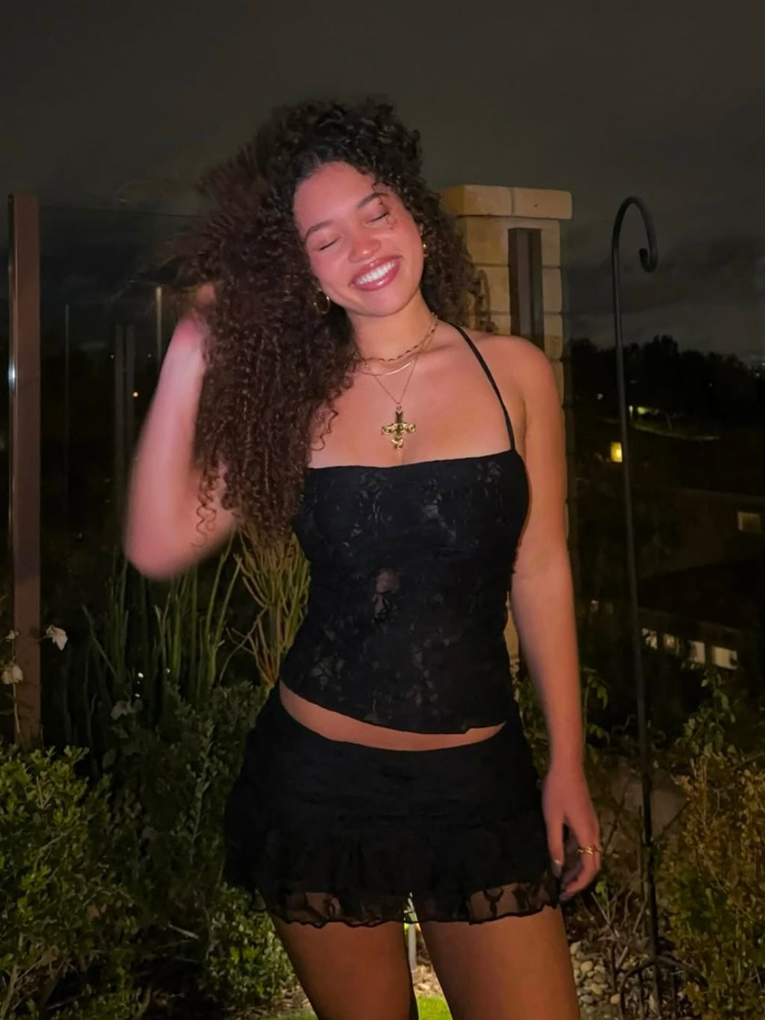 Model wearing a matching black lace set from Yasmin The Label featuring a halter top with adjustable ties at the top and back, and a mini skirt with built-in shorts; intricate lace fabric with triple-layered coverage on bust area, double-layered throughout; model is an Australian size 6 and wears XS/S in both pieces.