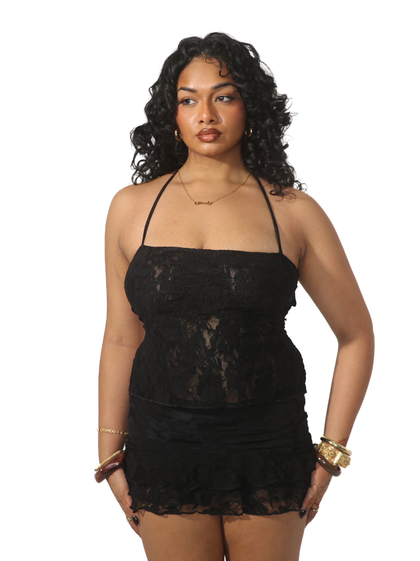 Model wearing a matching black lace set from Yasmin The Label featuring a top with adjustable ties and mini skirt with built-in shorts; triple-layered lace on bust area for coverage, double-layered throughout; model is size 10-12 and wears M/L.