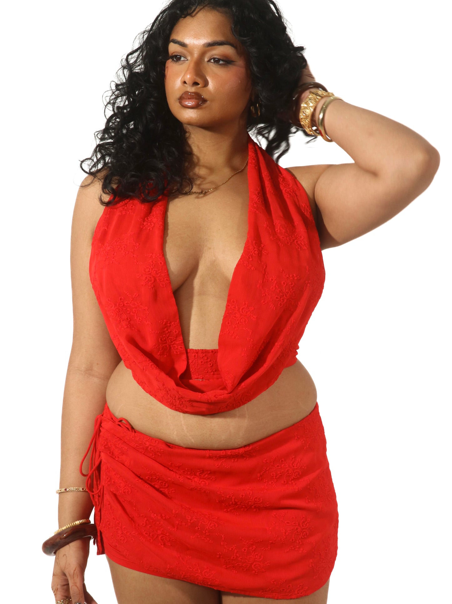 Model wearing a matching red set from Yasmin The Label featuring a scoop neck top with adjustable ties at the top and back, and a mini skirt with inbuilt shorts and embroidered pattern; skirt designed to sit low waisted with two ties at the side for adjustability; clean minimalist design shown on model who is an Australian size 10-12 and wears M/L in both pieces.