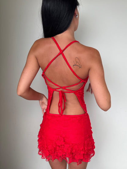 Model wearing a matching red lace set from Yasmin The Label featuring a top with adjustable ties and mini skirt with built-in shorts; triple-layered lace on bust area for coverage, double-layered throughout; model is size 6 and wears XS/S.