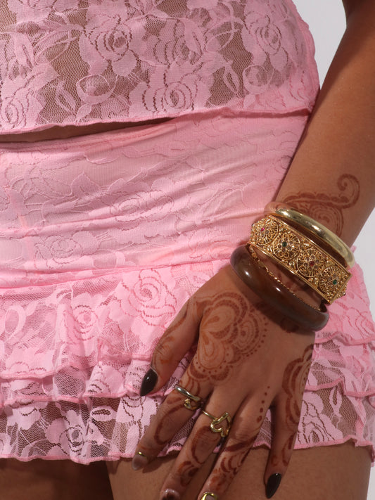 Model wearing a matching baby pink lace set from Yasmin The Label featuring a top with adjustable ties and mini skirt with built-in shorts; triple-layered lace on bust area for coverage, double-layered throughout; model is size 10-12 and wears M/L.