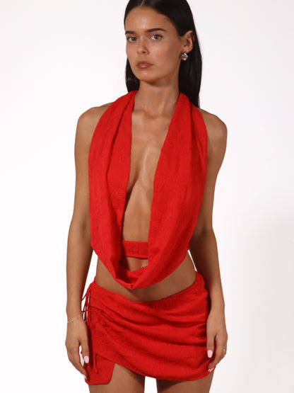 Model wearing a matching red set from Yasmin The Label featuring a scoop neck top with adjustable ties at the top and back, and a mini skirt with inbuilt shorts and embroidered pattern; skirt designed to sit low waisted with two ties at the side for adjustability; clean minimalist design shown on model who is an Australian size 6 and wears XS/S in both pieces.